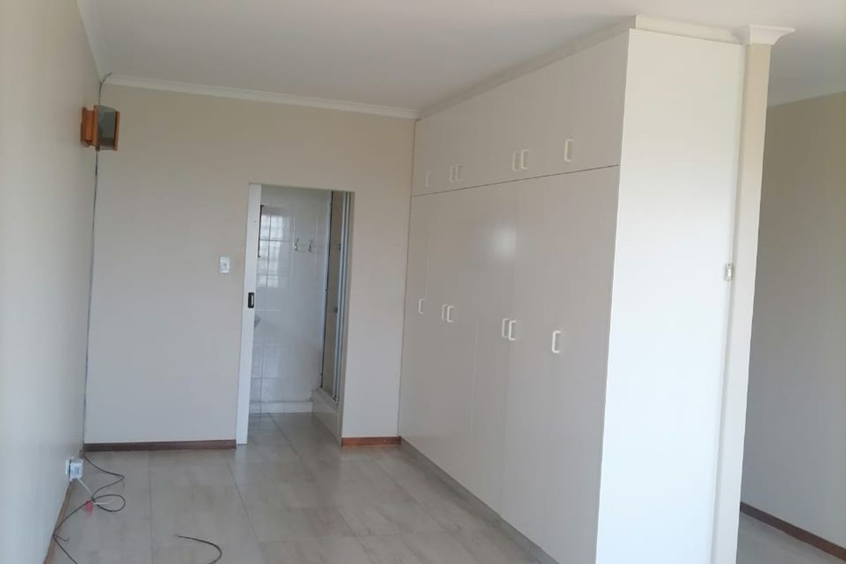 A bright, empty bedroom featuring neutral tiled flooring, ample built-in cupboard storage, and a doorway leading to an en-suite bathroom.