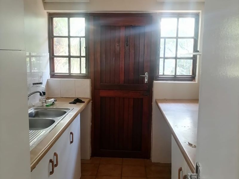 A functional scullery area featuring double stainless steel sinks, laminate countertops, ample built-in cabinetry, and a classic wooden stable door leading outdoors.