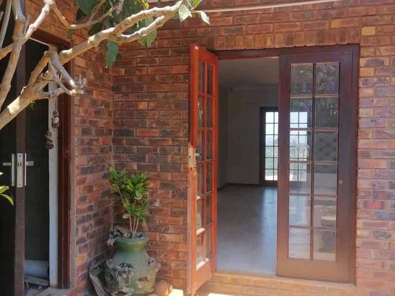 A covered patio area featuring exposed brick walls and classic wooden french doors leading into the interior living space.