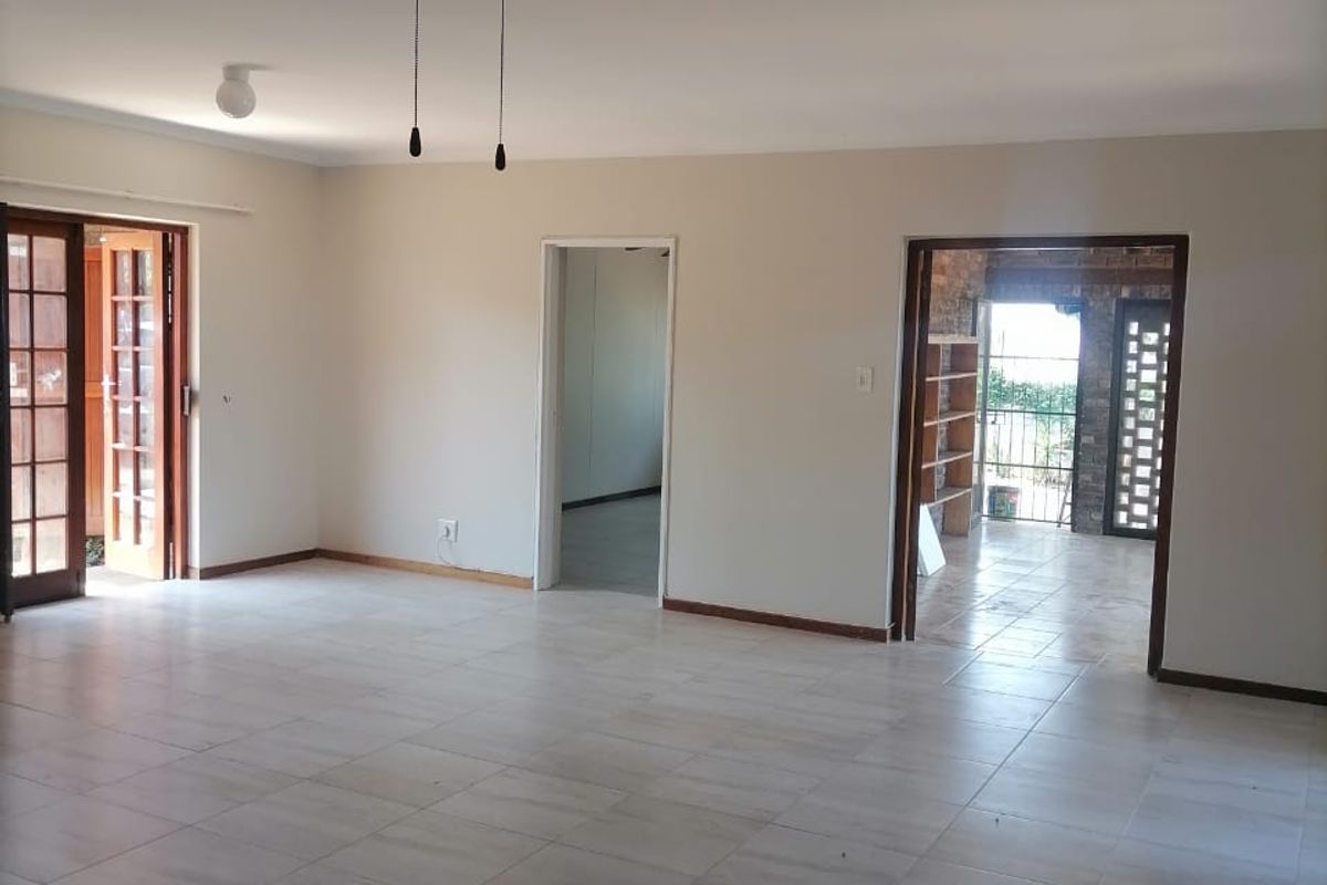 Spacious, empty living area featuring neutral tiled flooring, a ceiling fan, and multiple doorways leading to adjacent rooms and outdoor access.