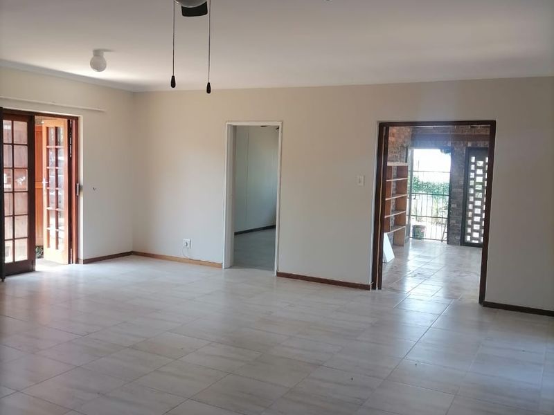 Spacious, empty living area featuring neutral tiled flooring, a ceiling fan, and multiple doorways leading to adjacent rooms and outdoor access.