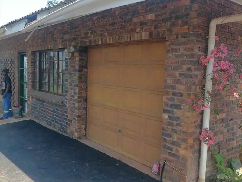 Exterior view of a face brick garage featuring a sectional door, guttering, and a side security gate entrance.