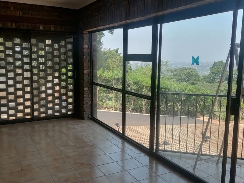 An enclosed balcony or sunroom featuring exposed brick walls, ceramic tile flooring, and large sliding glass doors with views of the surrounding landscape.