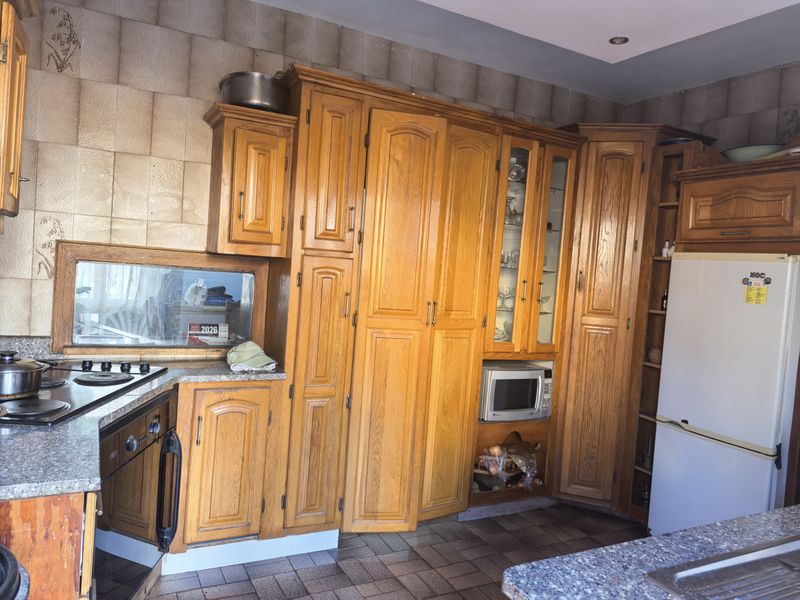 A traditional kitchen featuring extensive timber cabinetry, granite countertops, built-in appliances, and tiled splashbacks, offering a functional layout with potential for modern updates.