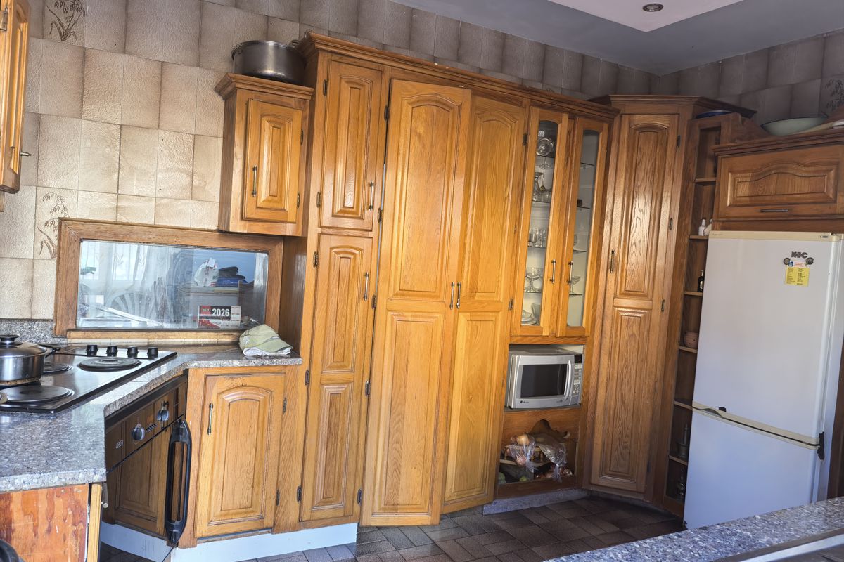 A traditional kitchen featuring extensive timber cabinetry, granite countertops, built-in appliances, and tiled splashbacks, offering a functional layout with potential for modern updates.