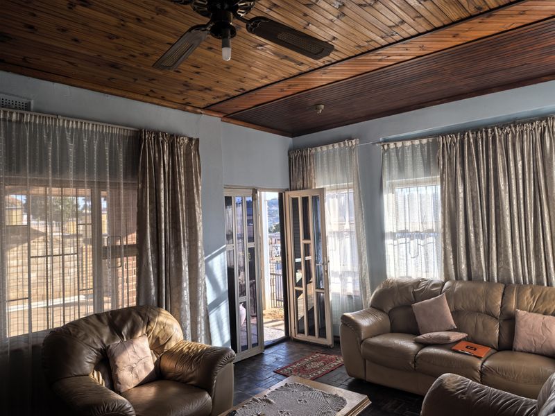 A living room featuring a timber tongue and groove ceiling, ceiling fan, tiled flooring, and access to an outdoor area through security gates.