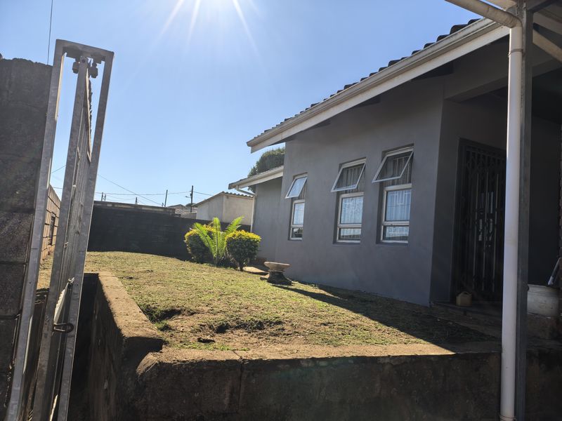 Rear exterior view of the house featuring a concrete retaining wall, lawn area, and security-fitted windows under a tiled roof.
