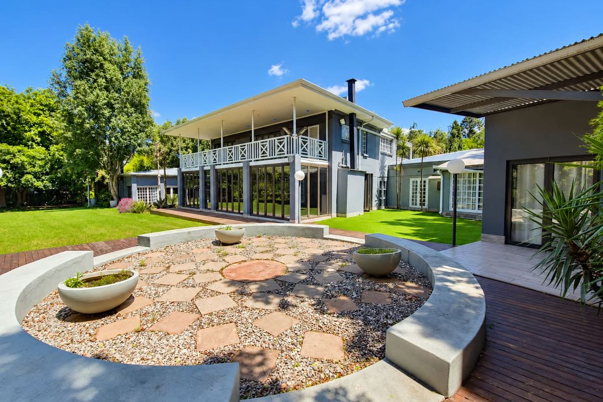 Spacious rear garden featuring a circular stone patio with built-in concrete seating, timber decking, and a two-story home with a covered balcony.