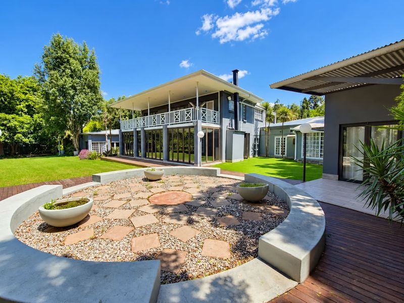 Spacious rear garden featuring a circular stone patio with built-in concrete seating, timber decking, and a two-story home with a covered balcony.