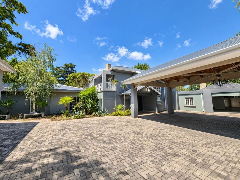 A well-maintained front exterior featuring a spacious paved driveway, a large covered carport, and a multi-level facade with a balcony.