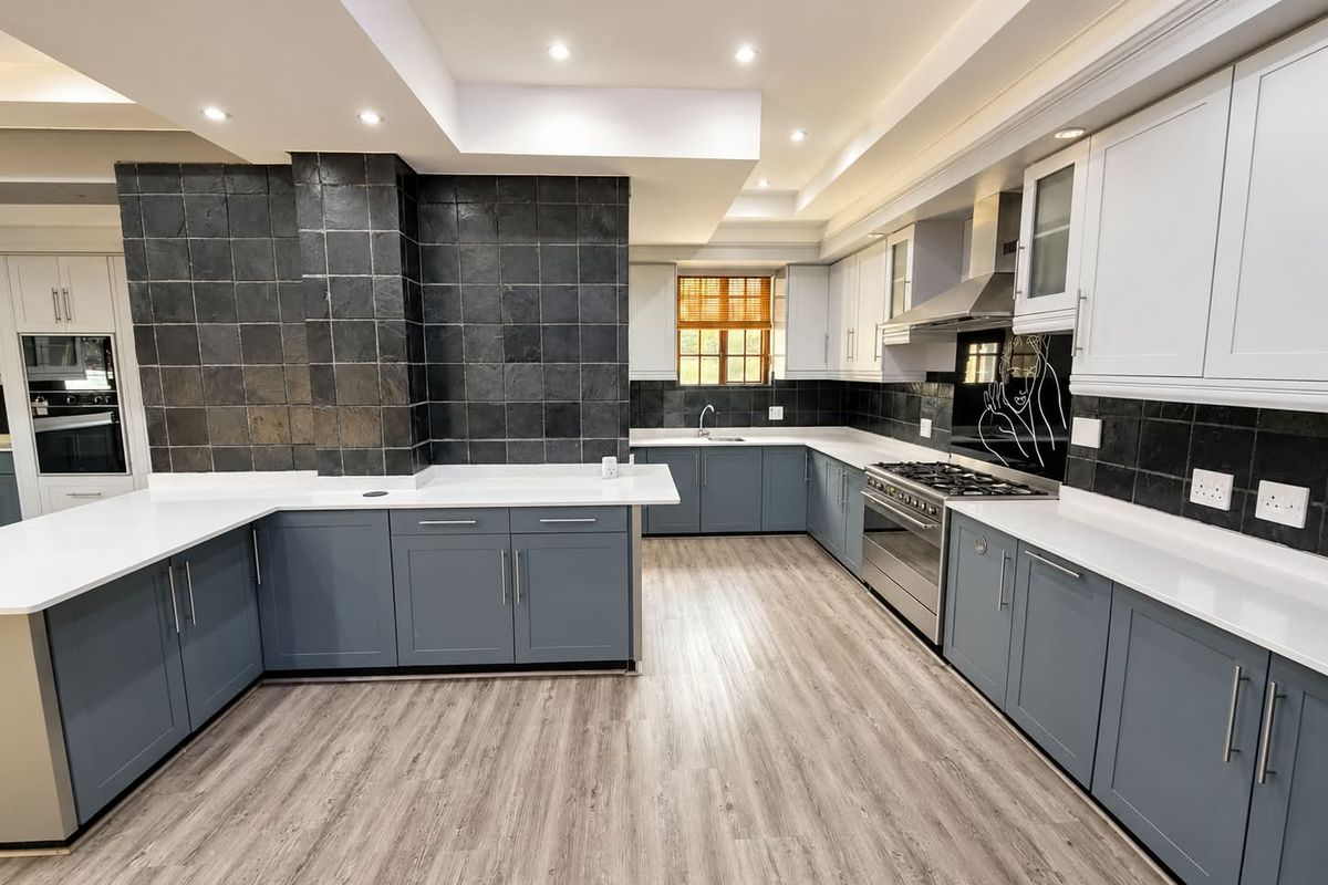 Modern, spacious kitchen featuring sleek grey cabinetry, white stone countertops, high-end gas hob, integrated oven, and stylish dark tiled splashbacks with recessed lighting.