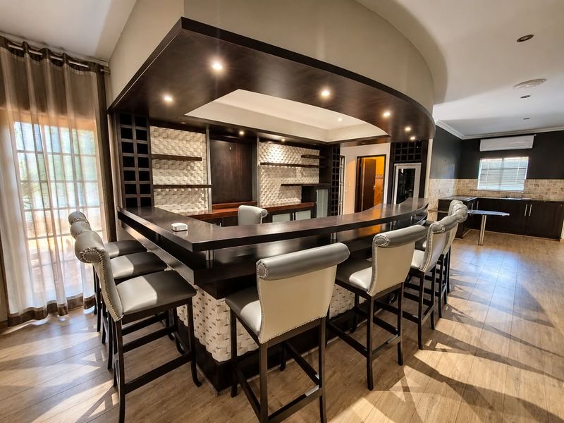 A well-appointed built-in bar area featuring a curved counter, recessed lighting, textured wall accents, and integrated wine storage, complemented by modern laminate flooring.
