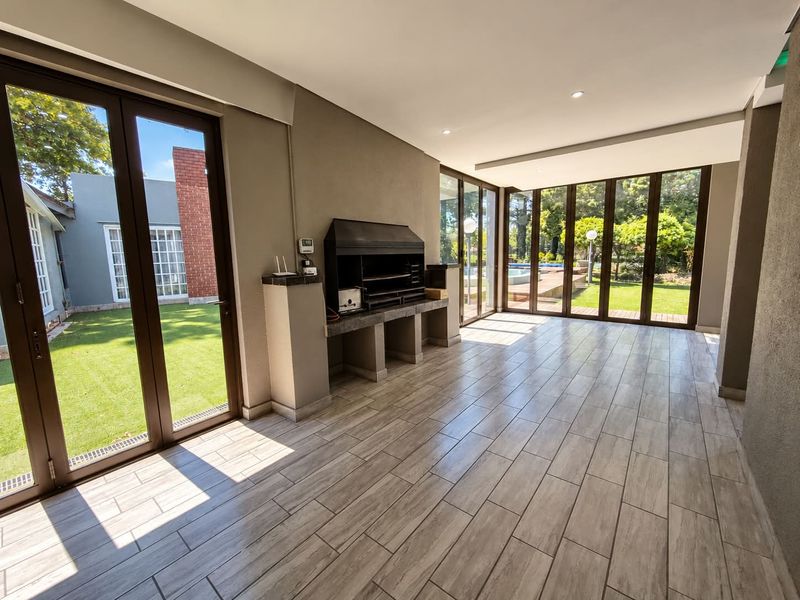 Spacious covered patio featuring a built-in braai, modern tiled flooring, and large aluminium stack doors opening onto the garden and pool area.
