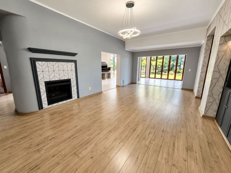 Spacious living room featuring light wood laminate flooring, a modern fireplace with geometric tile surround, and large bi-fold doors opening to the garden.