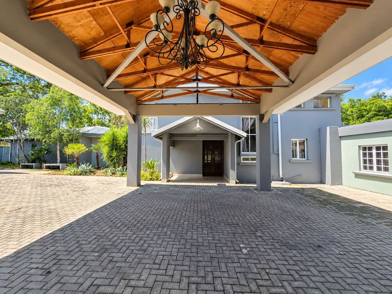 A spacious covered entrance area featuring exposed timber roof trusses, a paved driveway, and a grand front door, providing a welcoming approach to the home.