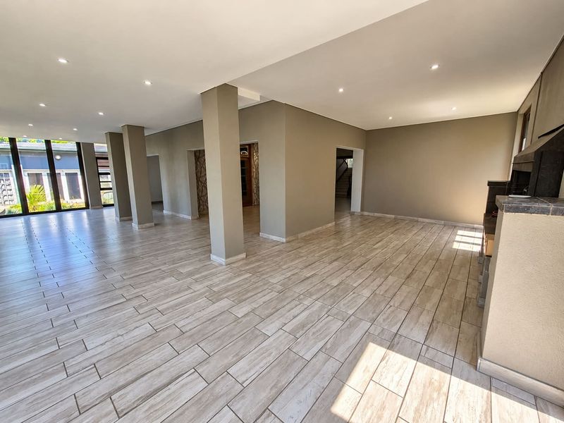 Spacious open-plan living area featuring modern tiled flooring, recessed downlighting, structural columns, and a built-in fireplace, offering a bright and versatile layout.