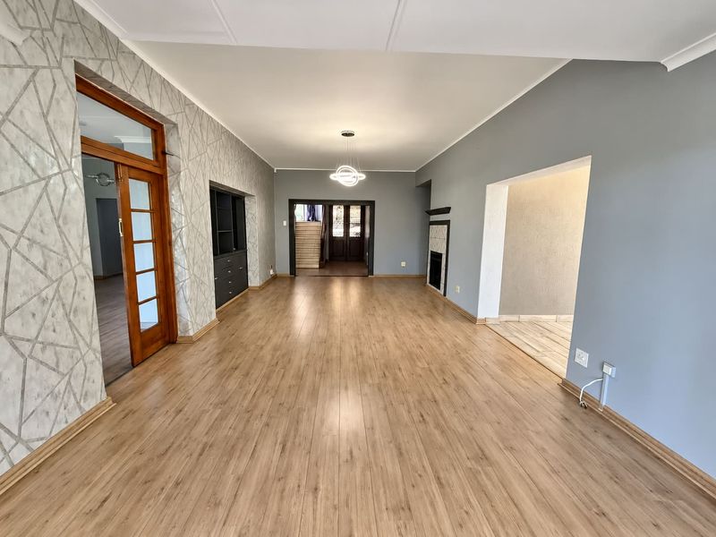 Spacious, light-filled living area featuring modern laminate flooring, a built-in fireplace, and contemporary pendant lighting, offering a versatile open-plan layout.