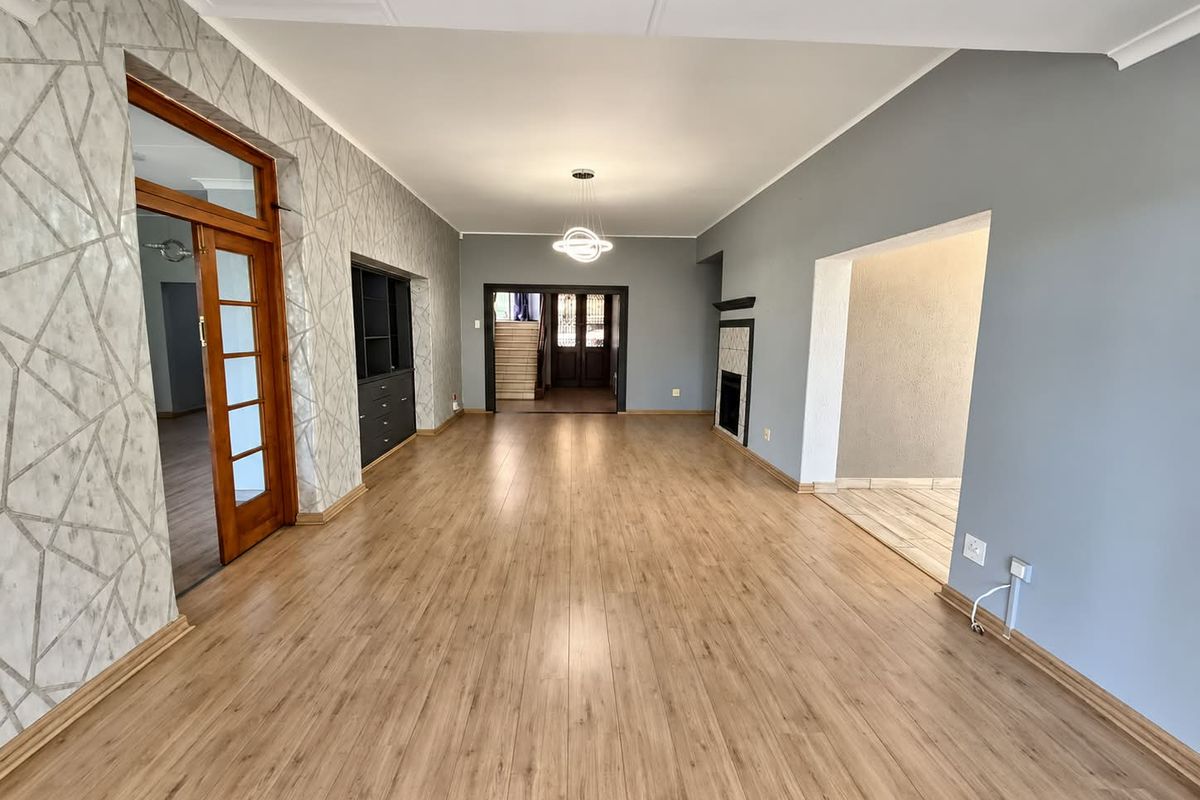 Spacious, light-filled living area featuring modern laminate flooring, a built-in fireplace, and contemporary pendant lighting, offering a versatile open-plan layout.