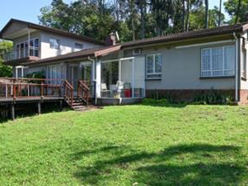 Rear view of the house featuring a raised timber deck, balcony, and a spacious garden area with established trees.