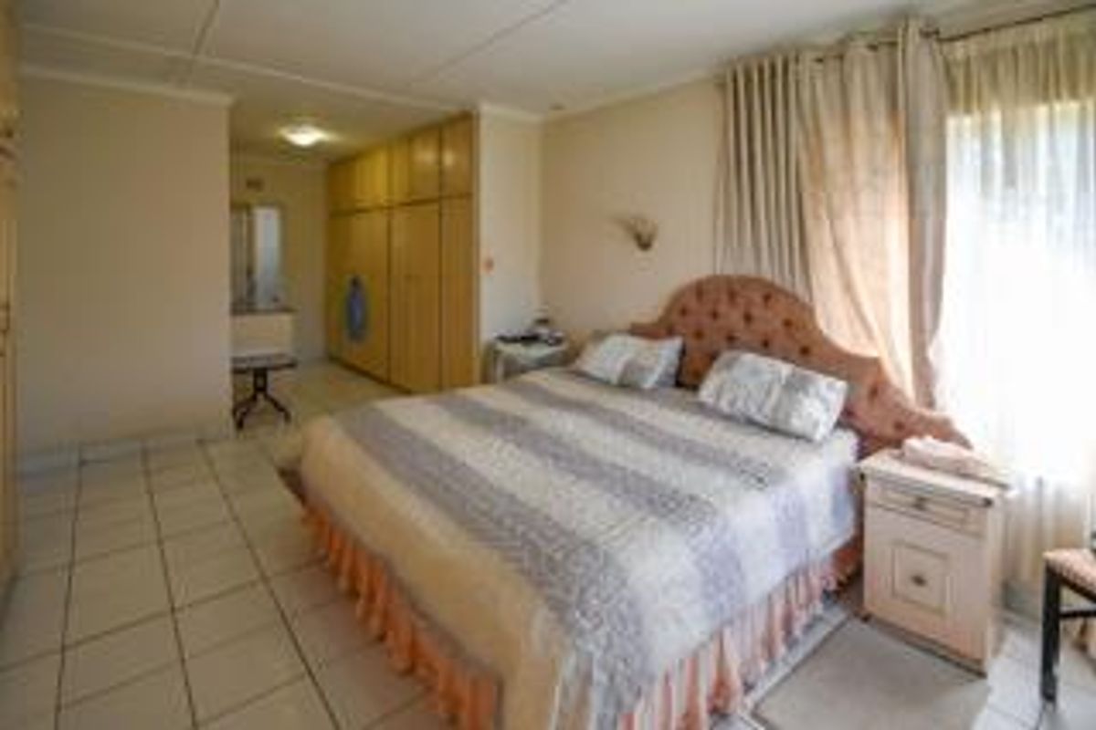 A spacious bedroom featuring tiled flooring and extensive built-in cupboards, offering ample storage space and natural light through large windows.
