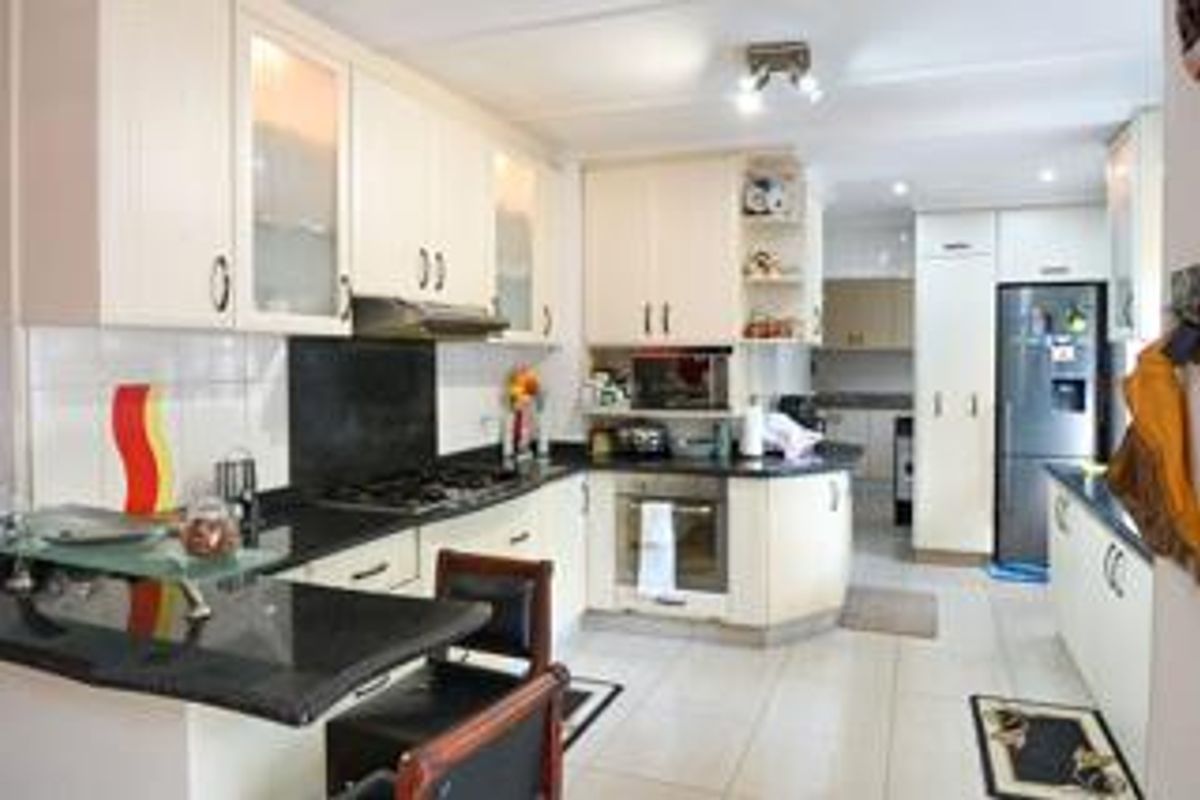 A functional kitchen featuring cream cabinetry, dark granite countertops, a gas hob, built-in oven, and a breakfast nook with tiled flooring.