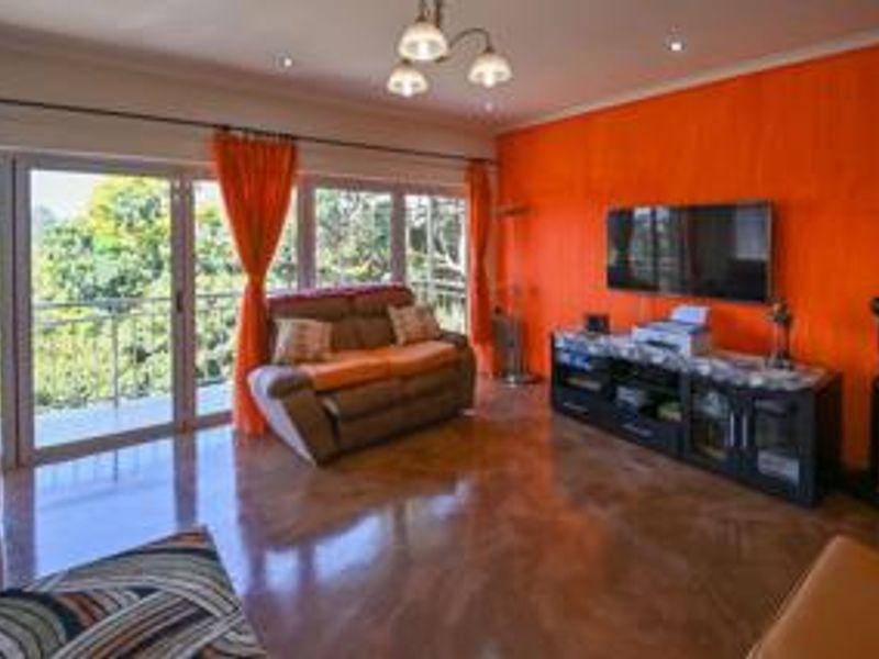Spacious living room featuring polished concrete floors, bright orange accent wall, and large sliding glass doors providing ample natural light and balcony access.