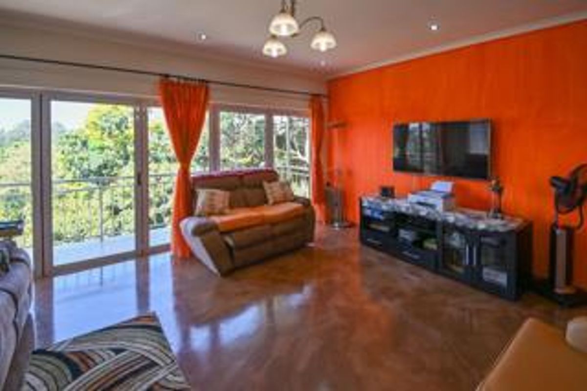 Spacious living room featuring polished concrete floors, bright orange accent wall, and large sliding glass doors providing ample natural light and balcony access.