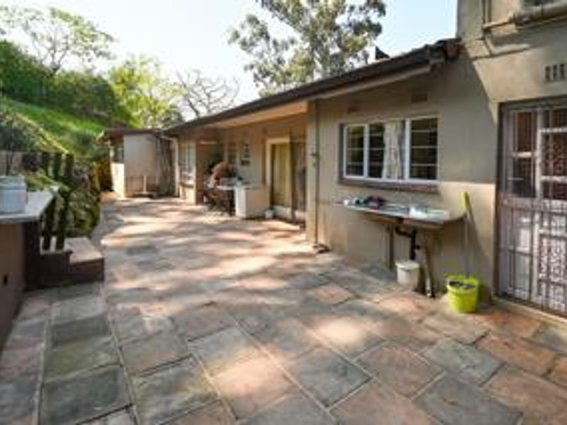 A spacious rear patio area featuring stone paving, an external sink, and direct access to the home through sliding glass doors.