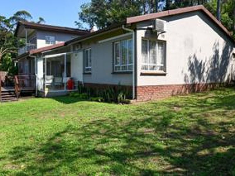 Rear view of the house featuring a brick plinth, timber deck, covered patio area, and established garden surroundings.