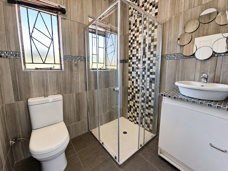 A functional bathroom featuring a glass shower enclosure, vessel sink with vanity cabinet, and tiled wall finishes with decorative accents.
