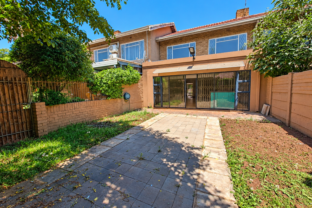 Rear view of a townhouse featuring a paved patio area, sliding glass doors with security gates, and a private garden space.