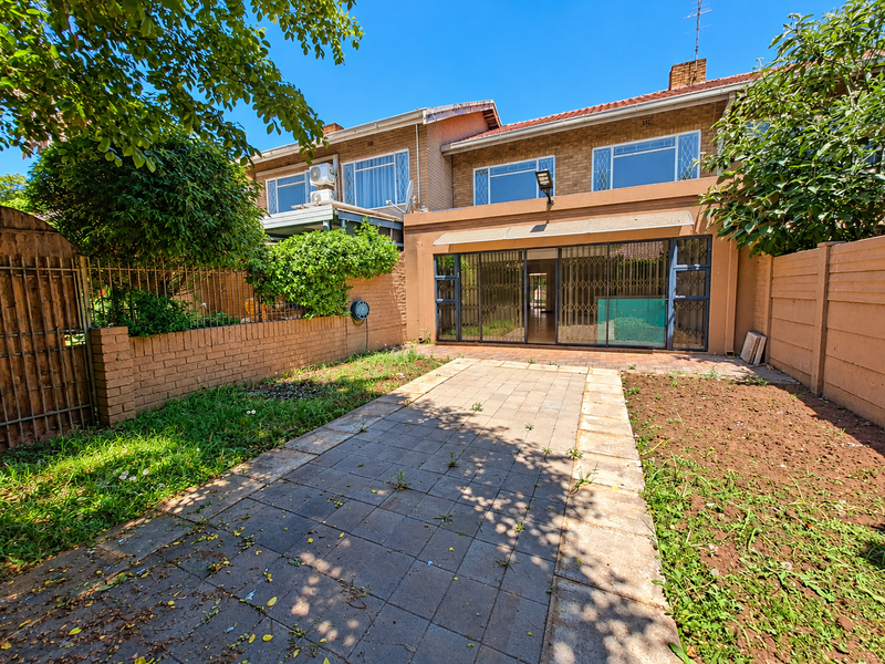 Rear view of a townhouse featuring a paved patio area, sliding glass doors with security gates, and a private garden space.