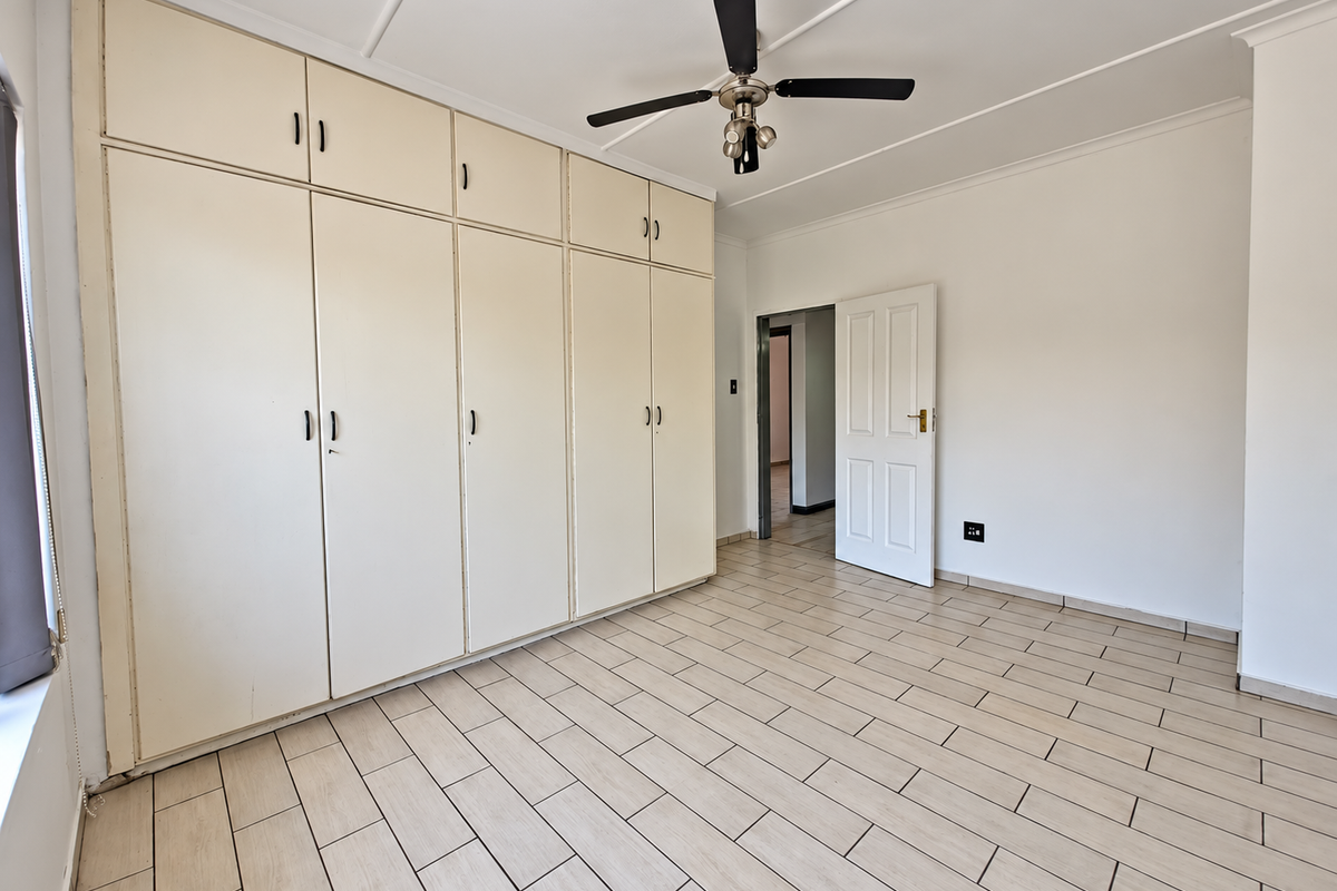 Spacious bedroom featuring extensive built-in cupboards, a ceiling fan, and neutral tiled flooring, offering a clean and functional blank canvas.