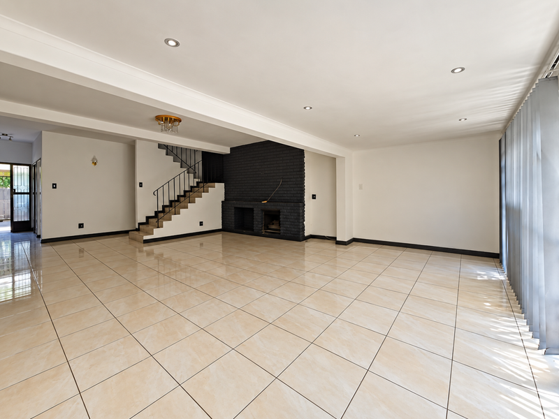Spacious, open-plan living area featuring large format floor tiles, a prominent black brick fireplace, and a staircase with a modern metal balustrade.