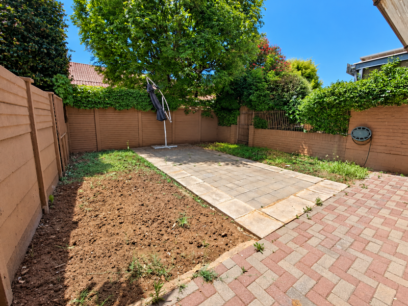 A private rear courtyard featuring a paved patio area, perimeter boundary walls, and garden beds requiring landscaping and maintenance.
