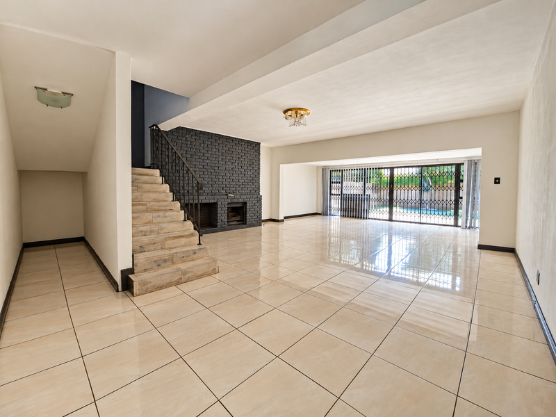 Spacious open-plan living area featuring large format floor tiles, a striking dark brick fireplace, and sliding doors leading to the outdoor pool area.