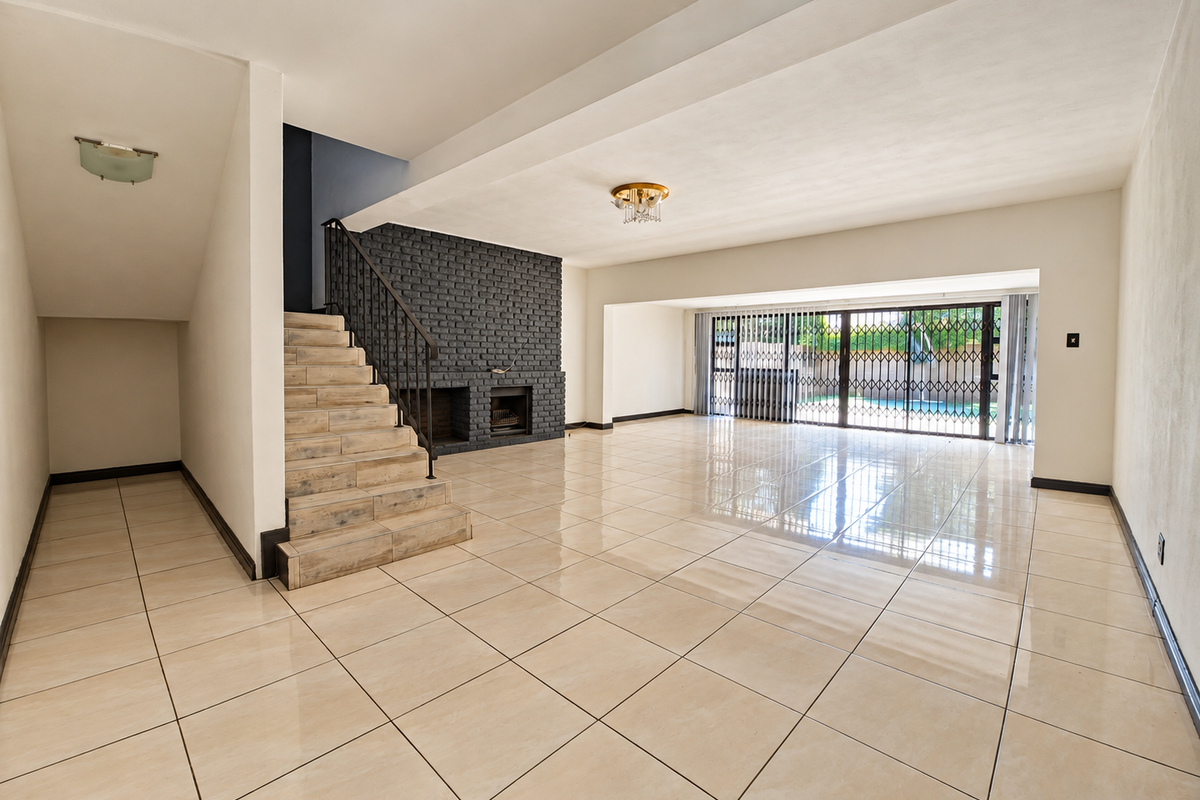 Spacious open-plan living area featuring large format floor tiles, a striking dark brick fireplace, and sliding doors leading to the outdoor pool area.
