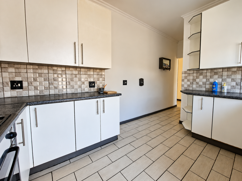 A functional kitchen featuring white built-in cabinetry, dark laminate countertops, a decorative tiled backsplash, and neutral ceramic floor tiles.