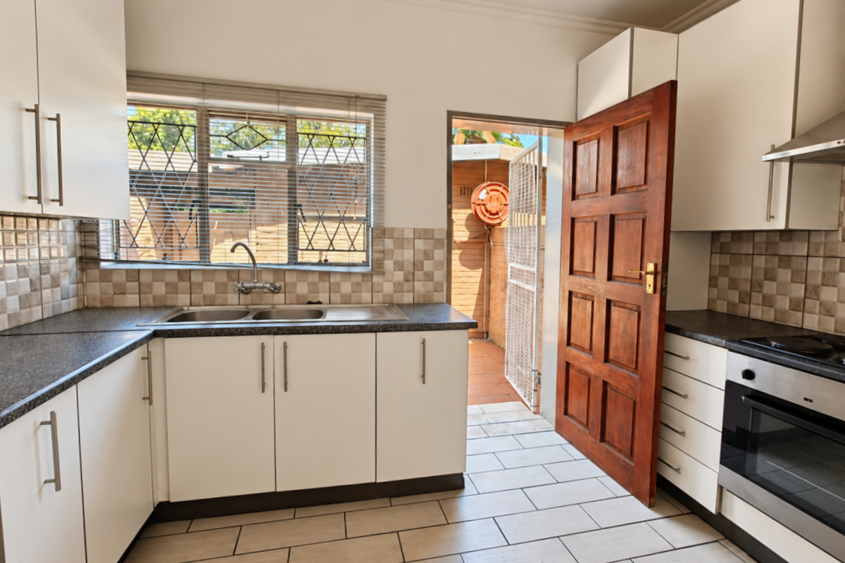Functional kitchen featuring white cabinetry, tiled splashbacks, built-in oven with extractor, and direct access to an outdoor area through a wooden door.