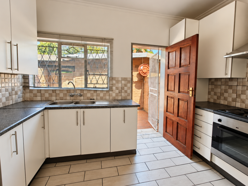 Functional kitchen featuring white cabinetry, tiled splashbacks, built-in oven with extractor, and direct access to an outdoor area through a wooden door.