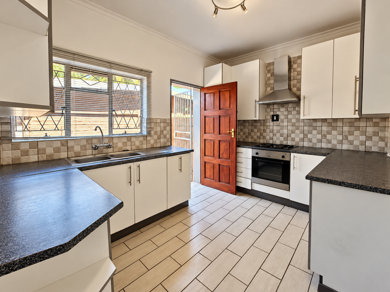 A clean, functional kitchen featuring white cabinetry, dark countertops, built-in oven with extractor fan, and tiled flooring with direct access to the exterior.