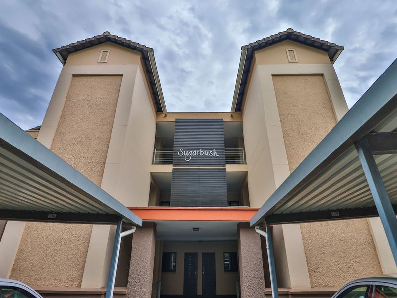 Front elevation of the Sugarbush apartment complex featuring covered parking bays and a multi-story residential facade.