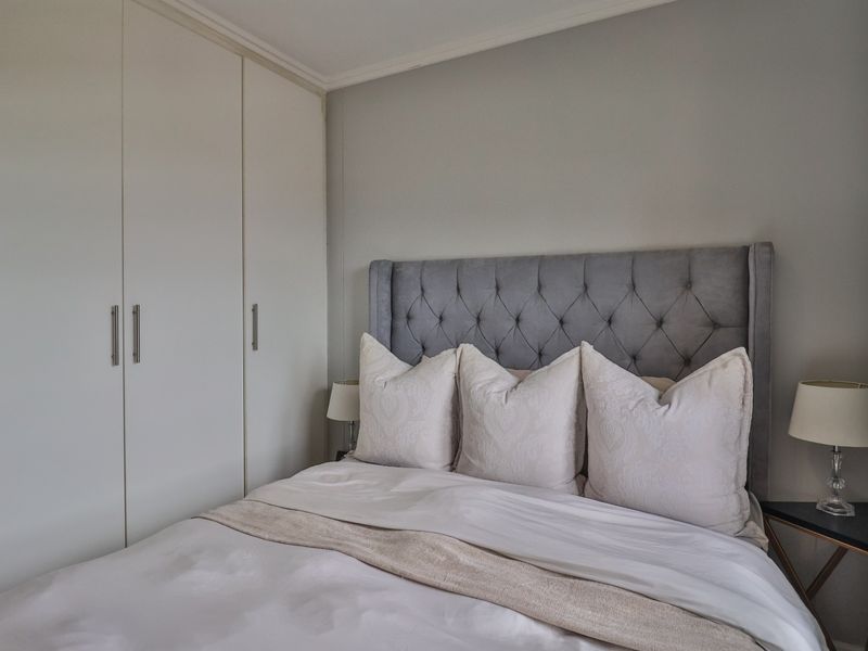 A well-maintained bedroom featuring neutral wall tones and practical floor-to-ceiling built-in cupboards for ample storage.