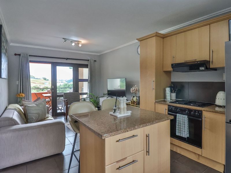Open-plan living area featuring a functional kitchen with light wood cabinetry, granite countertops, and direct access to a private balcony.