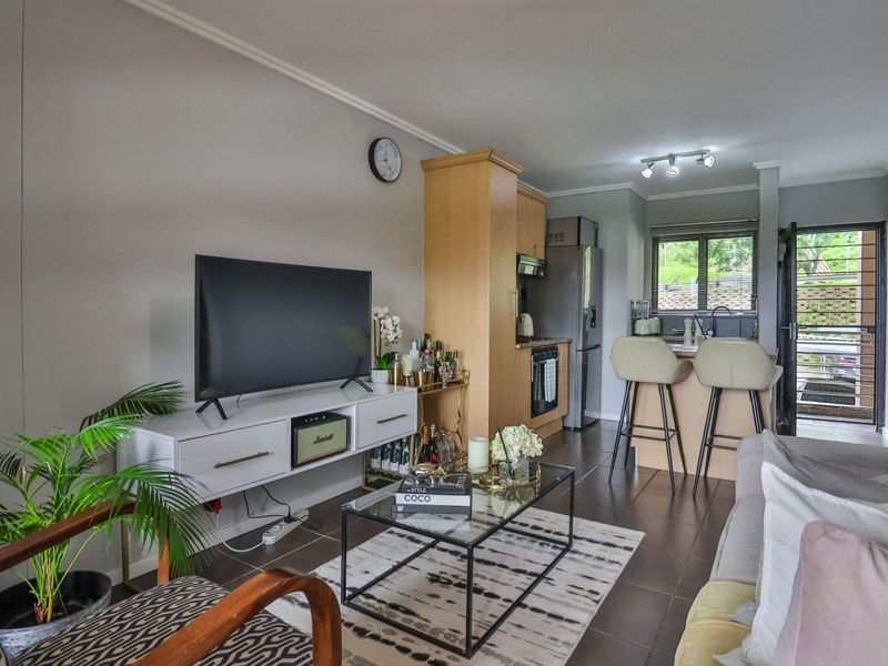An open-plan living and kitchen area featuring tiled flooring, a functional kitchen with built-in cabinetry, and a breakfast counter leading to an exterior door.