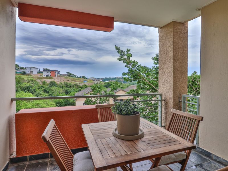 A covered balcony featuring tiled flooring and metal railings, offering scenic views of the surrounding landscape and residential area.