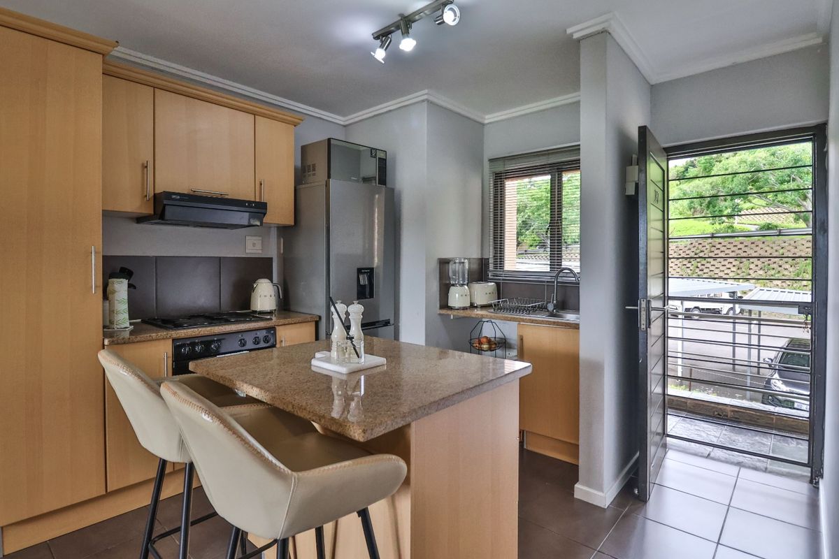 A functional kitchen featuring light wood cabinetry, granite countertops, a central island, and direct access to an exterior area through a security gate.
