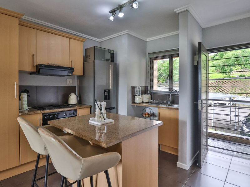 A functional kitchen featuring light wood cabinetry, granite countertops, a central island, and direct access to an exterior area through a security gate.