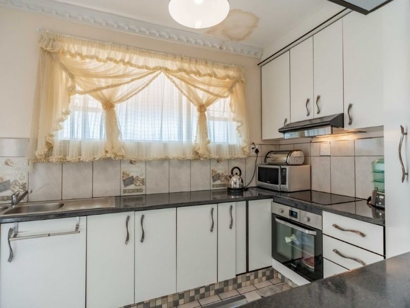 A functional kitchen featuring white cabinetry, dark countertops, tiled backsplash, and integrated appliances, with a visible water stain on the ceiling.
