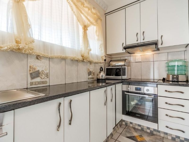 A functional kitchen featuring white cabinetry, dark laminate countertops, a built-in oven with hob, and a tiled backsplash.